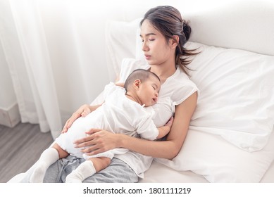 Being mom is so exhausted.  Tired mother laid in bed with newborn baby at night. Authentic real life exhausted parent taking rest with newborn child.
