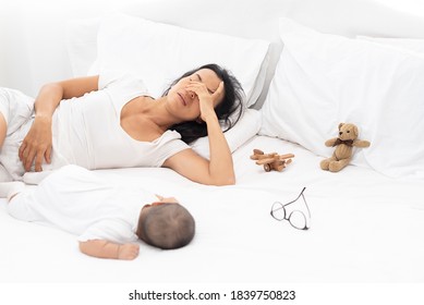 Being Mom Is So Exhausted.  Tired Mother Laid In Bed With Newborn Baby At Night. Authentic Real Life Exhausted Parent Taking Rest With Newborn Child.