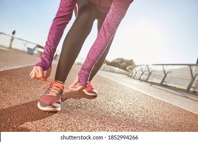 Being Prepared. Cropped Shot Of Active Mature Woman Wearing Sportswear Tying Her Shoe Laces While Getting Ready For Running Outdoors On A Sunny Day