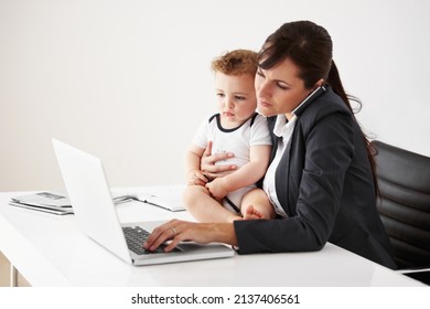 Being A Working Mom Is A Balancing Act. Working Mom Talking On The Phone While Holding A Baby And Typing On Her Laptop.