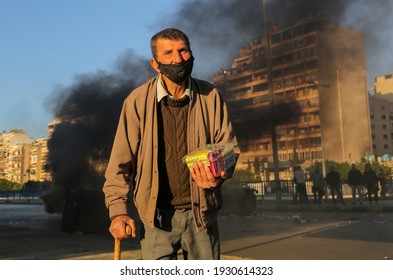 Beirut, Lebanon, March, 6, 2021: An elderly selling sweets pass in front of burning tires blocking a junction after the currency tumbled to a new low in a financial meltdown that has fueled poverty.  