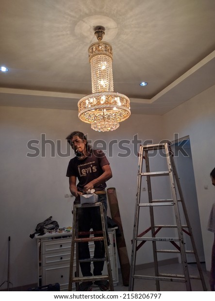 Bekasi, Indonesia, May 20,\
2022, One worker is installing a crystal decorative lamp in a\
room.
