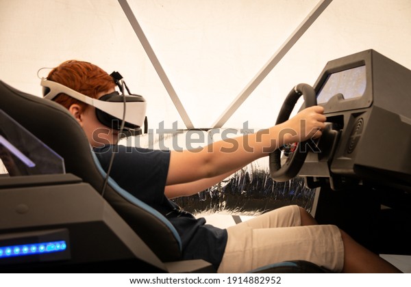 Belarus. Minsk\
07.20.2020 A boy wearing virtual reality glasses sits in a moving\
interactive car seat. The boy\'s hands are on the steering wheel.\
Virtual games. Virtual car\
driving.