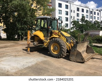 Belarus, Minsk,2022. A Yellow Tractor Stands On A Platform With A Wheel Being Removed Against The Backdrop Of A City