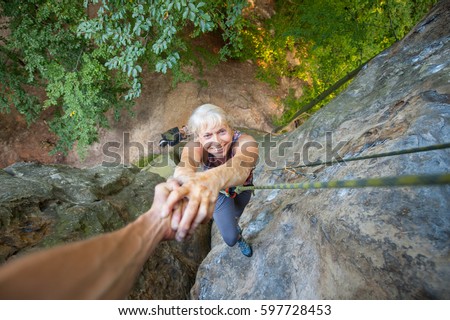 Belayer rockclimber is helping to older woman climber to reach a top of the rock. Man giving a helping hand to the woman