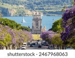 Belem Tower, Jacaranda Blooming Purple Blue Trees and Sailing Boat on Sunny Day. Lisbon, Portugal.