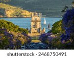 Belem Tower, Jacaranda Blooming Purple Blue Trees and Sailboats on Sunny Evening. Golden Hour. Lisbon, Portugal.