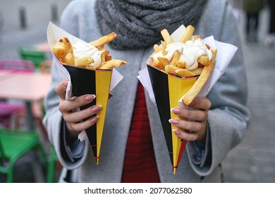 Belgian frites or french fries with mayonnaise in Brussels, Belgium. Female tourist holds two portions of fries in hands in the street.
