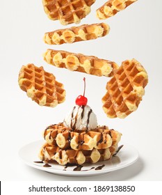 Belgian Liege Waffles With Ice Cream Ball And Chocolate Sauce, Cherry On Top And Levitation Waffles Around Plate Isolated On White Background. Side View.