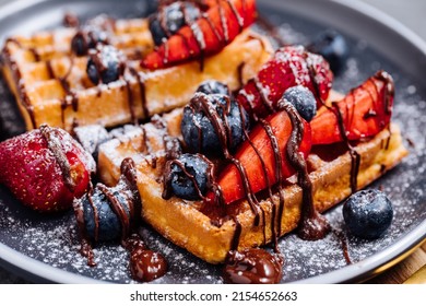 Belgian waffle with chocolate, strawberry, blueberries and powdered sugar on dark plate - Powered by Shutterstock