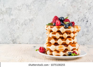 Belgian waffles with raspberries, blueberries and syrup, homemade healthy breakfast, light concrete background copy space