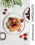 Belgian waffles sprinkled with powdered sugar with strawberries and cherries top view on a white background with copy space