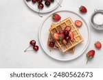 Belgian waffles sprinkled with powdered sugar with strawberries and cherries top view on a white background with copy space