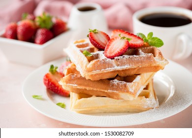 Belgian waffles with strawberry and powdered sugar on white plate, pink background