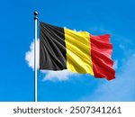 Belgium flag flying on blur blue clouds background.