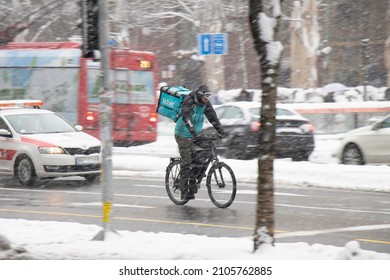 Belgrade, Serbia - January 11, 2022: Winter City Traffic In Heavy Snow Storm, And One Wolt Delivery Courier Riding A Bicycle On City Street