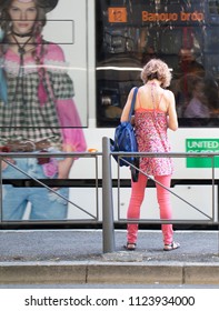 Belgrade, Serbia - June 1, 2018 : One Blond Women In Casual Pink Outfit Standing At A Bus Stop And Waiting For Public Transportation On A Sunny Spring Day And A Tram Moving Past With A Fashion Ad