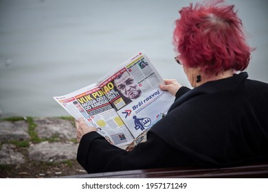 BELGRADE, SERBIA - MARCH 18, 2017: Old Woman Sitting On A  Bench Reading The Serbian Tabloid Newspaper Informer With Governmental Propaganda For The SNS Serbian Progressive Party. 

