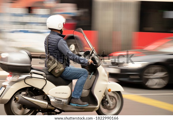 Belgrade,\
Serbia - September 25, 2020: Mature man riding beige scooter on\
busy city street, with vehicles in motion\
blur
