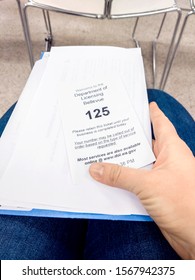 Bellevue, WA / USA - Circa November 2019: Person Holding Their Waiting Number Ticket And License Documents In The Waiting Area Of The Bellevue DMV.