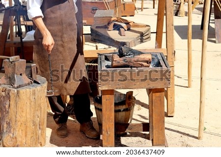  Bellows inflate the fire in the coals. Master Blacksmith in Blacksmith Workshop Demonstrating Old Technologies at the Festival of Living History in Torres Vedras, Portugal. 