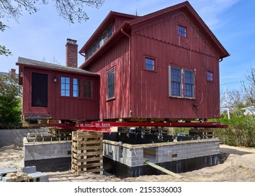 Bellport, NY USA - May 1, 2022: An old red wood house has been raised on piers and a new cinderblock foundation is being built underneath to raise the house above flood level.
