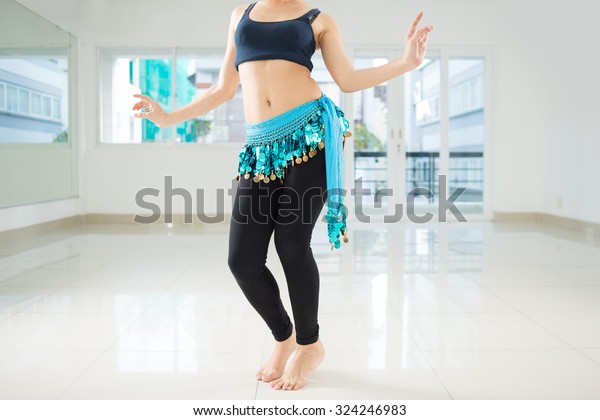 Belly dancer in legging and hip scarf dancing in\
the class