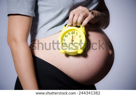 Belly of a pregnant woman with alarm clock