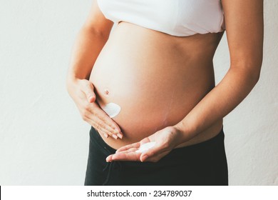 Belly of a pregnant woman applying moisturizer