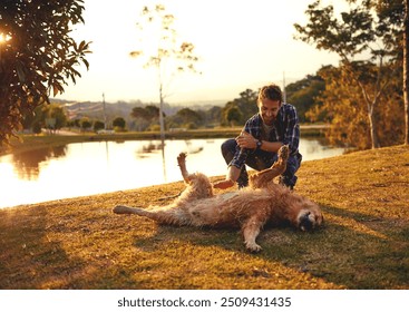 Belly rub, outdoor and man with dog, nature and relax with golden retriever, bonding and together. Massage, pet and person with smile, playing and fun with animal, water and lake in woods and game - Powered by Shutterstock