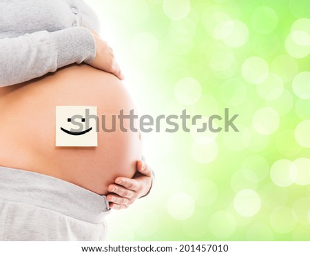 Belly of a young pregnant woman with a white sticker and a smiley on it