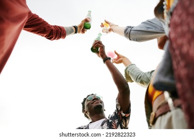 Below angle of young happy intercultural friends cheering up with bottles of beer and cocktails while enjoying outdoor party - Powered by Shutterstock