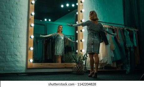 From below back view of beautiful singer in short sparkling dress and gloves standing in front of mirror practicing show