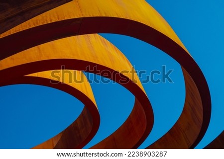From below exterior of modern building with sunlit rings on top located against cloudless blue sky in city