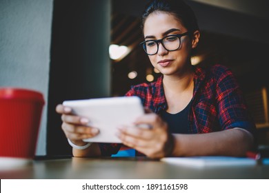From below of focused ethnic woman browsing tablet and looking attentively on screen while working remotely in modern cafe at daytime and drinking coffee - Powered by Shutterstock
