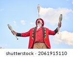 From below man in red costume balancing club on nose while juggling against cloudy blue sky during performance in park