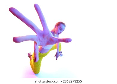 From below portrait of attractive young woman wearing trendy sport outfit in neon light while reaching out hands towards camera. Concept of sport, fashion, active lifestyle, youth, ad. Copy space