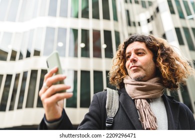 From Below Self Assured Mature Male With Curly Hair Reading Message On Cellphone While Standing Against Modern Building In Downtown