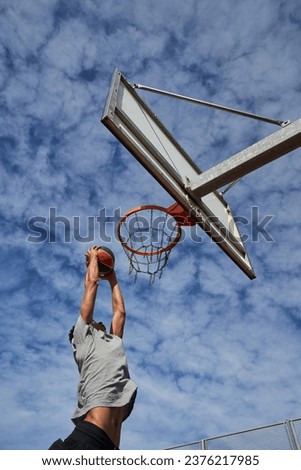 From below side view of sportive guy in activewear doing slam dunk on outdoor sports ground during basketball workout