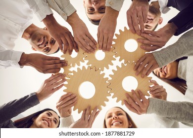 From below of team of young creative multicultural people joining gear wheels together as metaphor for effective teamwork, unity, collaboration, finding working solution and creating business system