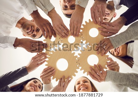 From below of team of young creative multicultural people joining gear wheels together as metaphor for effective teamwork, unity, collaboration, finding working solution and creating business system