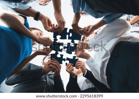 Below view of diverse corporate officer workers collaborate in office connecting puzzle pieces as partnership and teamwork concept. Unity and synergy in business idea by merging jigsaw puzzle. Concord