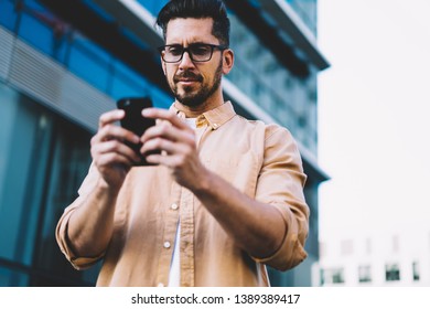 Below View Of Handsome Man In Eyeglasses Concentrated On Updating Profile For Social Networks Connected To Wireless For Browsing Application With Information, Ordering Taxi Cab Via App