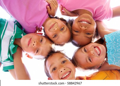 Below view of happy children embracing each other and smiling at camera