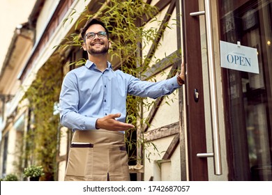 Below view of happy waiter inviting customers to come in while opening a new cafe.  - Powered by Shutterstock