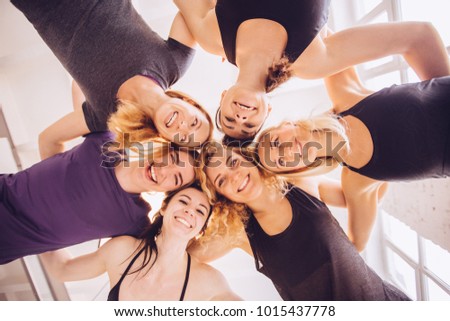 Below view of laughing sportive women in sportswear looking at camera with white interior studio above them.