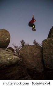 From Below View Of Sportive Man Jumping From Rock To Rock Doing Parkour In Dark Night. 