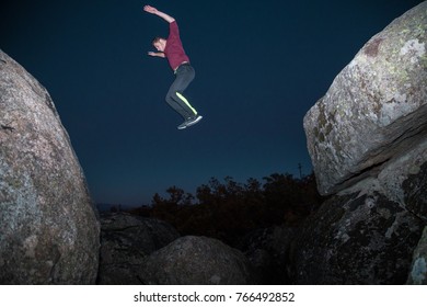 From Below View Of Sportive Man Jumping From Rock To Rock Doing Parkour In Dark Night. 