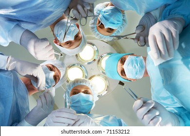 Below view of surgeons holding medical instruments in hands and looking at patient
