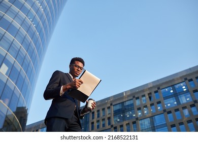 Below view of thoughtful young black businessman in elegant suit walking over business district and examining papers on move - Powered by Shutterstock